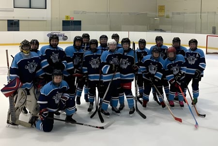 Eine Gruppe von Hockeyspielern der St. Kevin's High School posiert gemeinsam auf einer Eisbahn vor einem Tor.