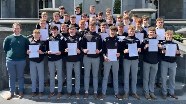 Eine Gruppe von Schülern des St. Kieran’s College steht vor einem akademischen Gebäude und hält stolz ihre Zertifikate.