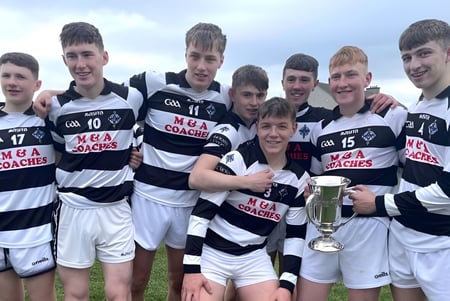 Eine Gruppe Schüler des St. Kieran’s College steht mit einer Sporttrophäe auf einem Rasenfeld unter bewölktem Himmel.