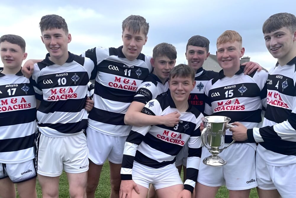Eine Gruppe Schüler des St. Kieran’s College steht mit einer Sporttrophäe auf einem Rasenfeld unter bewölktem Himmel.