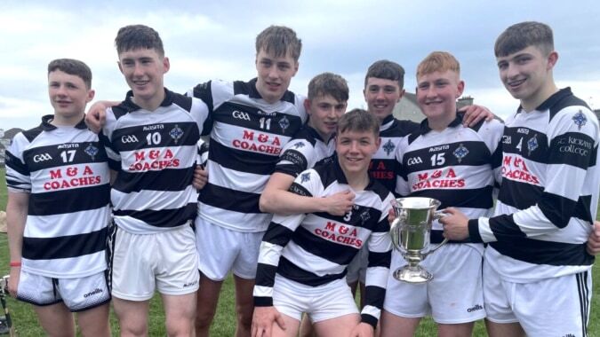 Eine Gruppe von Schülern des St. Kieran’s College steht mit einem Pokal auf einem Sportfeld unter bewölktem Himmel.