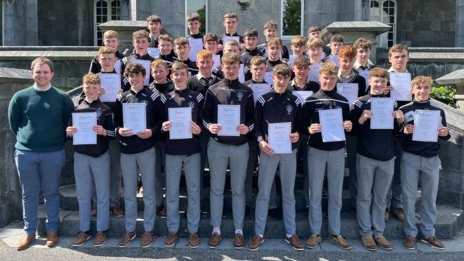 Eine Gruppe von Schülerinnen und Schülern des St. Kieran’s College steht vor einem steinernen Gebäude und hält stolz Zertifikate hoch.