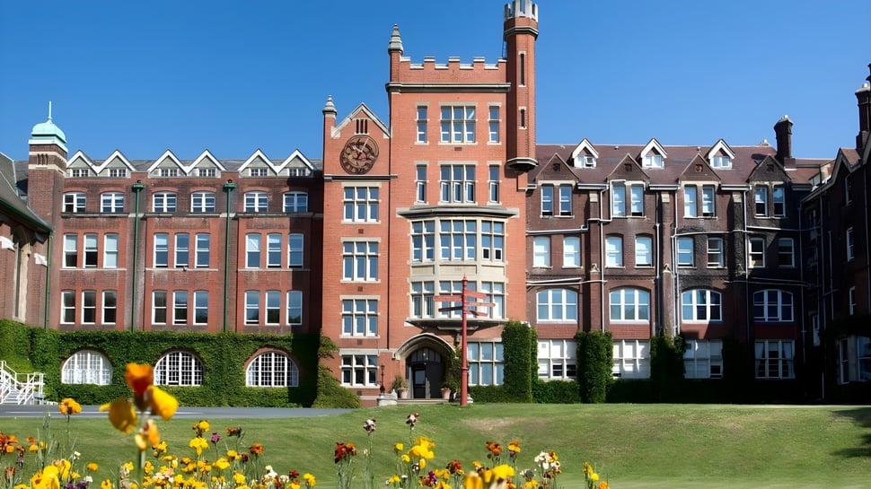 Das Hauptgebäude des St. Lawrence College mit einem hohen Turm steht hinter einer grünen Wiese mit gelben Blumen.