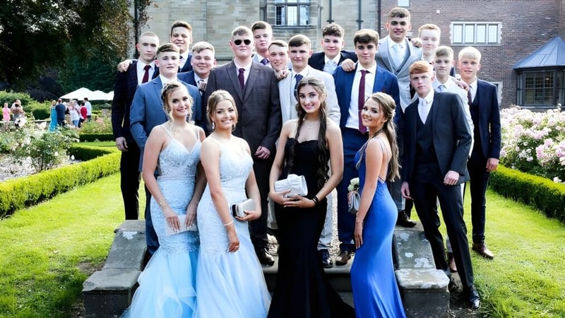 Eine Gruppe von formell gekleideten Personen auf dem Campus des St. Lawrence College vor einem grünen Garten.