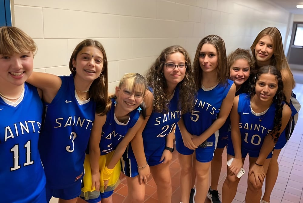 Eine Gruppe junger Basketballspielerinnen in blauen Saints-Uniformen auf dem Flur der St. Lawrence Secondary School.
