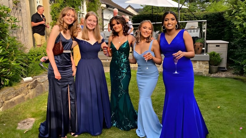 Fünf Schülerinnen des St. Leo’s College stehen in eleganten Abendkleidern im Garten vor einer Steinmauer.