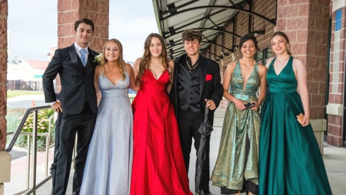 Sechs Personen in formeller Kleidung stehen auf einem Balkon der St. Louis Community School vor einer Backsteinwand.