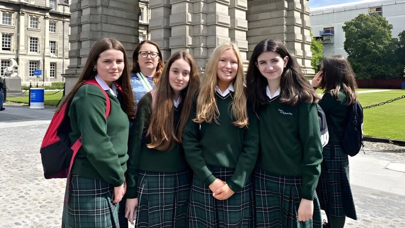 Eine Gruppe von Schülerinnen in grüner Schuluniform steht vor einem großen, verzierten Steingebäude auf dem Campus der St. Louis Community School.