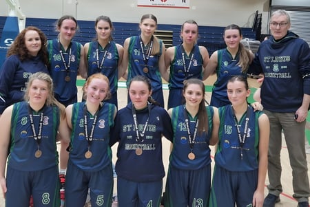 Eine Gruppe junger Athletinnen in Sportuniform posiert vor einem Basketballplatz auf dem Campus der St. Louis Secondary School.