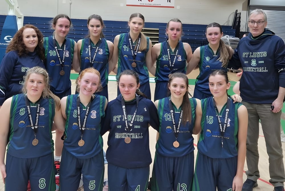 Eine Gruppe junger Athletinnen in Sportuniform posiert vor einem Basketballplatz auf dem Campus der St. Louis Secondary School.