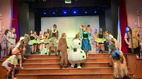 Eine Gruppe von Schülern der St. Louis Secondary School steht in bunten Kostümen auf der Bühne vor einem bemalten Bühnenbild.