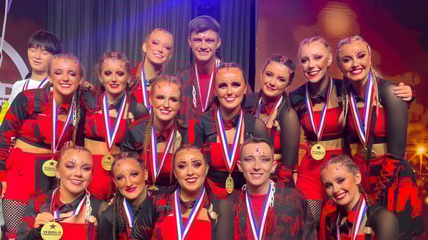 Eine Gruppe von Schülerinnen und Schülern der St. Louis Secondary School Dundalk posiert in roten und schwarzen Kostümen auf der Bühne.