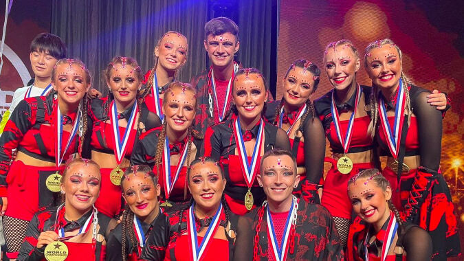Schülerinnen und Schüler der St. Louis Secondary School in Dundalk posieren in auffälligen Kostümen auf der Bühne mit buntem Bühnenlicht.