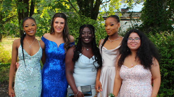 Vier Schülerinnen der St. Louis Secondary School in Dundalk posieren gemeinsam in einer grünen Außenanlage mit Bäumen im Hintergrund.