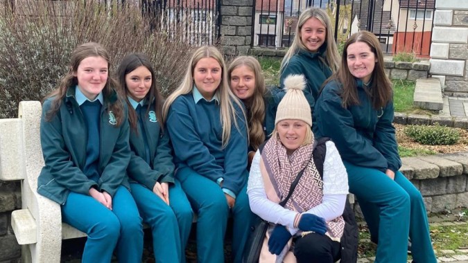 Eine Gruppe von Schülerinnen der St. Louis Secondary School posiert gemeinsam vor einer Steinmauer und einem Holzzaun.