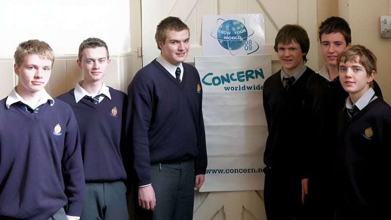 Eine Gruppe Schülerinnen und Schüler steht vor dem Banner von CONCERN worldwide auf dem Campus von St. Macartan's College.