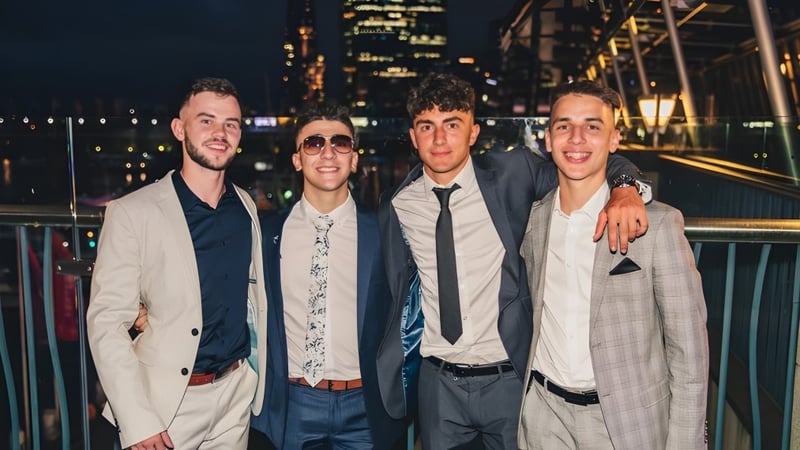 Vier Schüler des St. Macartan's College posieren gemeinsam vor einer nächtlichen Stadtkulisse mit beleuchteten Hochhäusern.