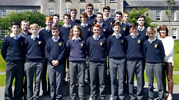 Eine Gruppe von Schülern in Schuluniformen steht auf dem Rasen vor einem Backsteingebäude des St. Macartan's College.