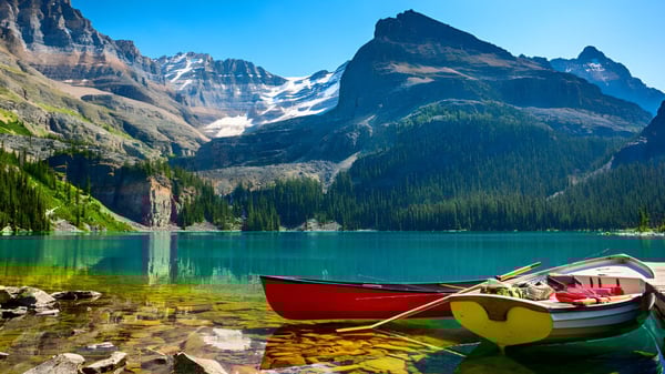 Ein ruhiger alpiner See mit einem roten und gelben Boot vor schneebedeckten Bergen auf dem Gelände der St. Margaret’s School.