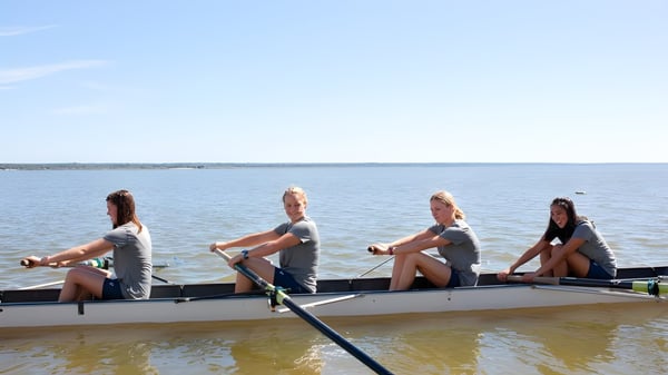Vier Personen sitzen in einem Boot auf dem Wasser auf dem Campus der St. Margaret's School bei klarem Himmel.