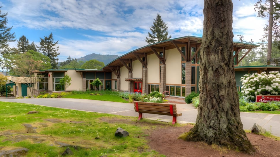 Ein holzhaus im Lodge-Stil steht auf dem Gelände der St. Margaret’s School umgeben von hohen Kiefern und Bergen im Hintergrund.