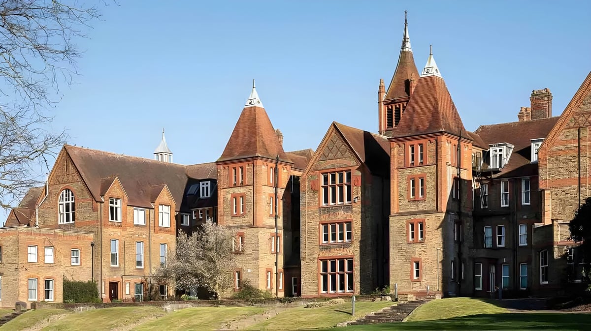 Das historische Backsteingebäude mit verzierten architektonischen Details auf dem Campus der St. Margaret’s School ist von grüner Vegetation umgeben.