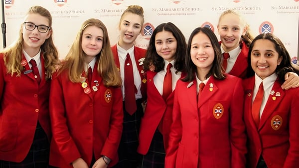 Eine Gruppe von Schülerinnen und Schülern der St. Margaret’s School posiert in roten Uniformen vor einem Logo-Hintergrund.