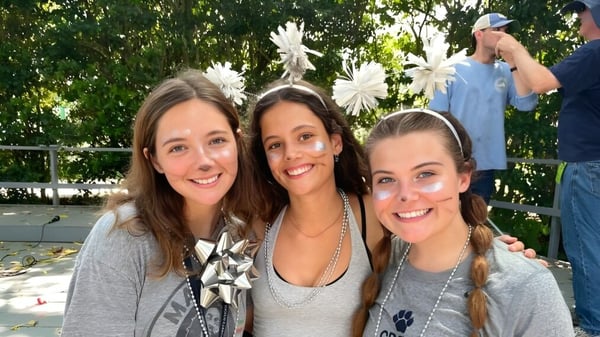 Drei Schülerinnen der St. Margaret's School posieren draußen vor grünen Bäumen und Sträuchern.