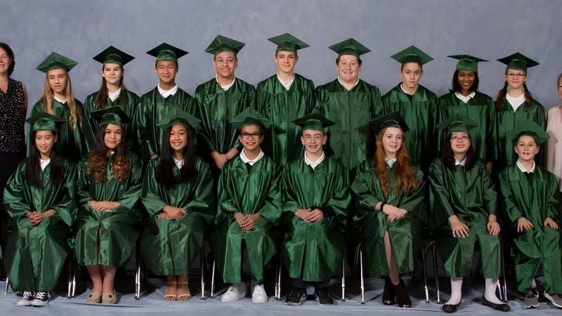 Eine Gruppe von Absolventen der St. Mark High School steht in grünen Talaren und Hüten vor einem grauen Hintergrund.
