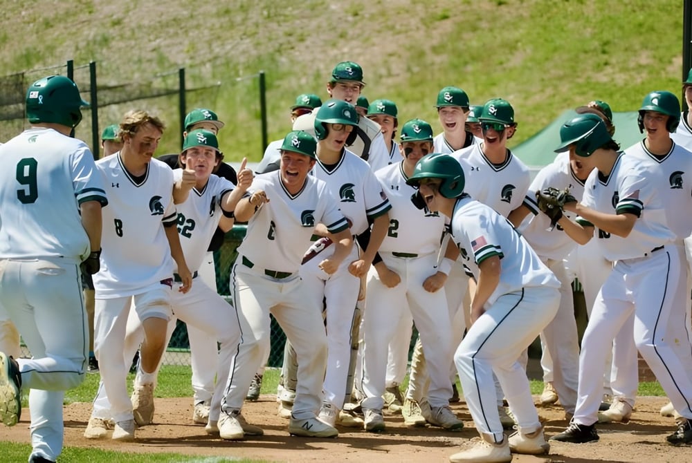 Eine Gruppe von Baseballspielern in weißen Uniformen mit grünen Helmen auf dem Baseballfeld der St. Mark High School.