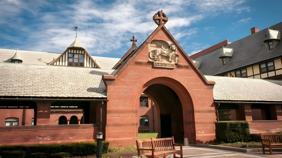 Das charakteristische Backsteingebäude der St. Mark's School mit spitzem Dach und Bogenportal ist von grüner Vegetation umgeben.