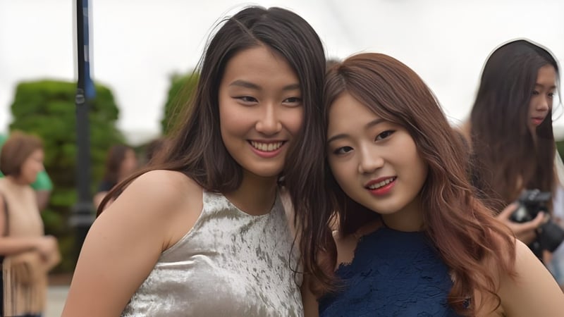 Zwei Schülerinnen mit langen dunklen Haaren lächeln gemeinsam vor Grünflächen auf dem Campus der St. Mark's School.