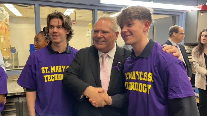 Drei Personen in violetten Shirts begrüßen einen älteren Mann im Anzug am St. Mary Catholic Secondary School.