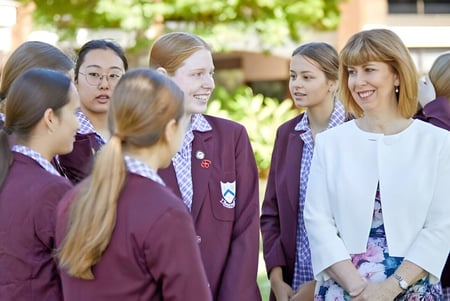 Eine Gruppe junger Schülerinnen steht auf dem Campus der St. Mary's Anglican Girls' School vor Bäumen und Schulgebäuden.
