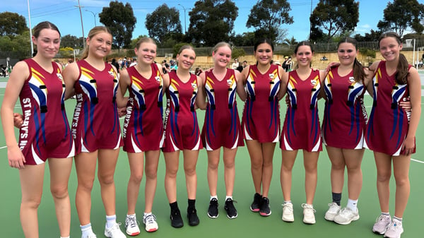 Eine Gruppe junger Sportlerinnen steht in roten und blauen Trikots gemeinsam auf dem Sportfeld der St. Mary's Anglican Girls' School.