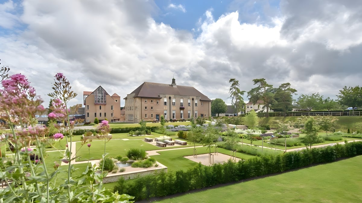 Das historische Gebäude von St. Mary's Calne ist von einem gepflegten Garten mit bunten Blumen und geschnittenen Hecken umgeben.