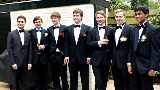 Eine Gruppe Schüler des St. Marys College Galway steht in formeller Kleidung vor einem Gebäude mit Holzfassade und Grünpflanzen.