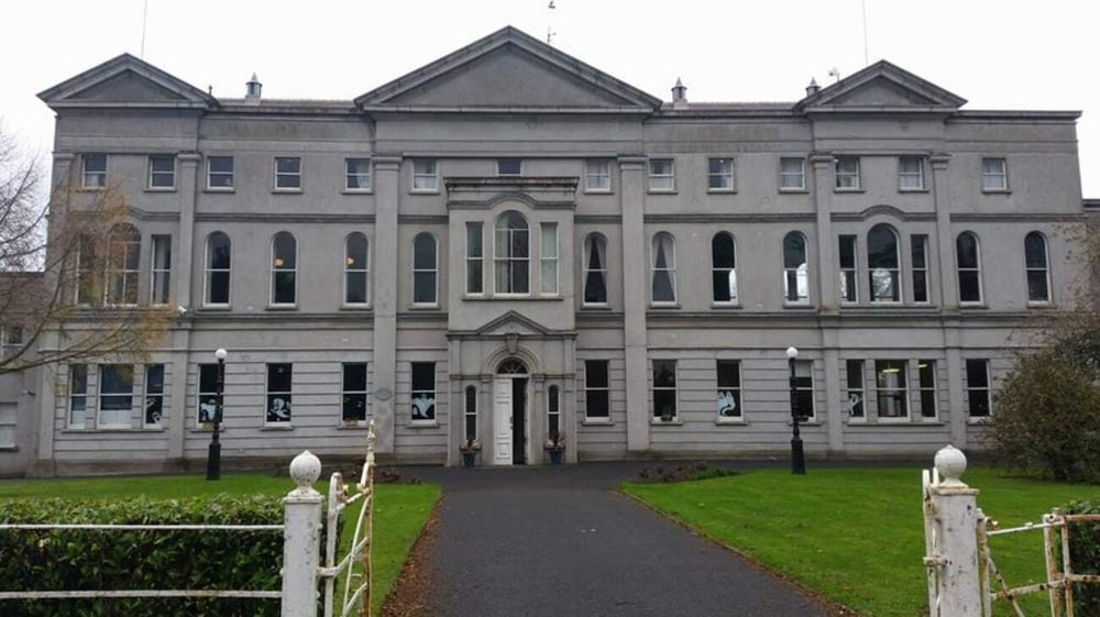 Das repräsentative Steingebäude mit symmetrischer Fassade auf dem Gelände des St. Mary’s College ist von Rasenflächen und einem Metallzaun umgeben.