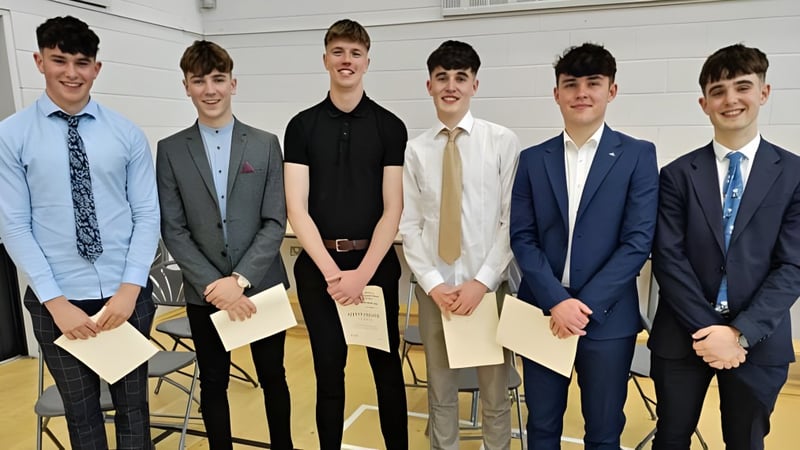 Eine Gruppe von sechs jungen Männern im Anzug steht zusammen vor weißem Hintergrund auf dem Campus von St. Mary’s College.