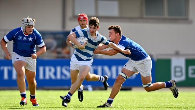 Schüler von St. Mary’s College spielen Rugby und ein Spieler wird beim Versuch, den Ball zu halten, von zwei Gegenspielern getackelt.