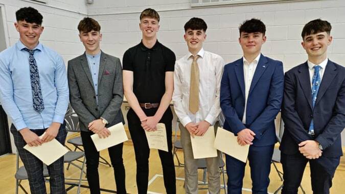 Sechs Schüler in formeller Kleidung stehen zusammen auf dem Campus von St. Mary’s College vor einer weißen Wand.