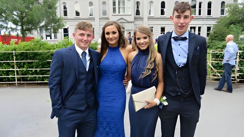 Vier Schülerinnen und Schüler in formeller Kleidung stehen vor einem historischen Gebäude auf dem Campus des St. Mary’s College.