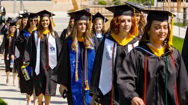 Eine Gruppe von Absolventinnen und Absolventen der St Mary’s District & Vocational Collegiate Institute steht in akademischer Kleidung auf dem Campus.