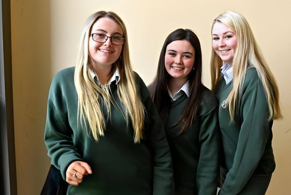 Drei Schülerinnen in grünen Schuluniformen stehen lächelnd zusammen auf dem Flur der St. Mary's Holy Faith Killester.
