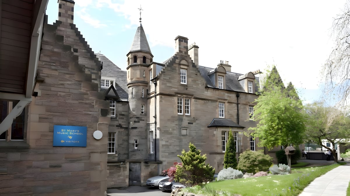 Das historische steinerne Gebäude der St. Mary’s Music School ist von grünen Pflanzen und einem gepflasterten Weg umgeben.