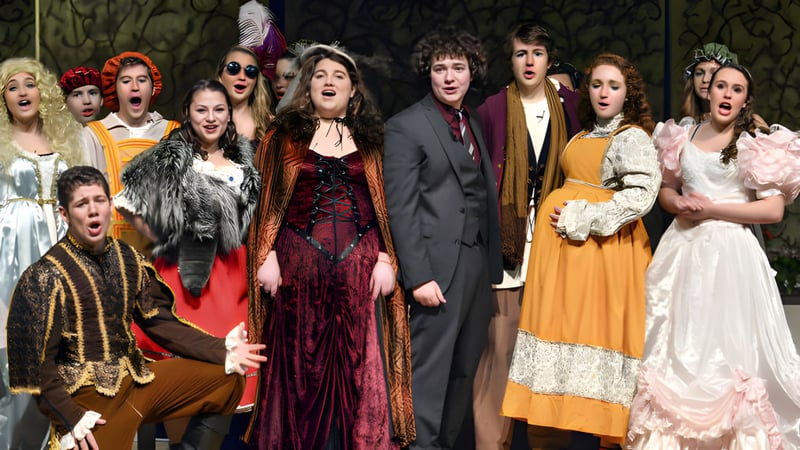 Schüler der St. Mary's Ryken High School führen ein Theaterstück in bunten Kostümen auf einer Bühne mit dunklem Hintergrund auf.