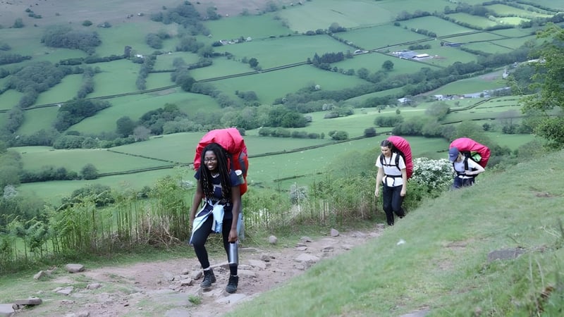 Drei Schülerinnen und Schüler der St. Mary’s School Ascot wandern auf einem Feldweg durch grüne Hügellandschaft.