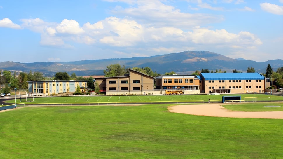 Ein grünes Feld vor dem modernen Gebäudekomplex auf dem Campus der St. Mary's School mit Bergen im Hintergrund.