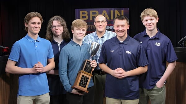 Eine Gruppe von sechs Schülern steht mit einem Pokal auf dem Campus der St. Mary's School vor einem Brain-Schild.