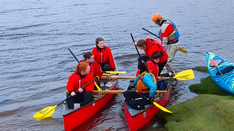 Eine Gruppe von Schülern der St. Mary’s Secondary trägt rote Schwimmwesten und befindet sich mit Kajaks auf einem Gewässer nahe dem Ufer.